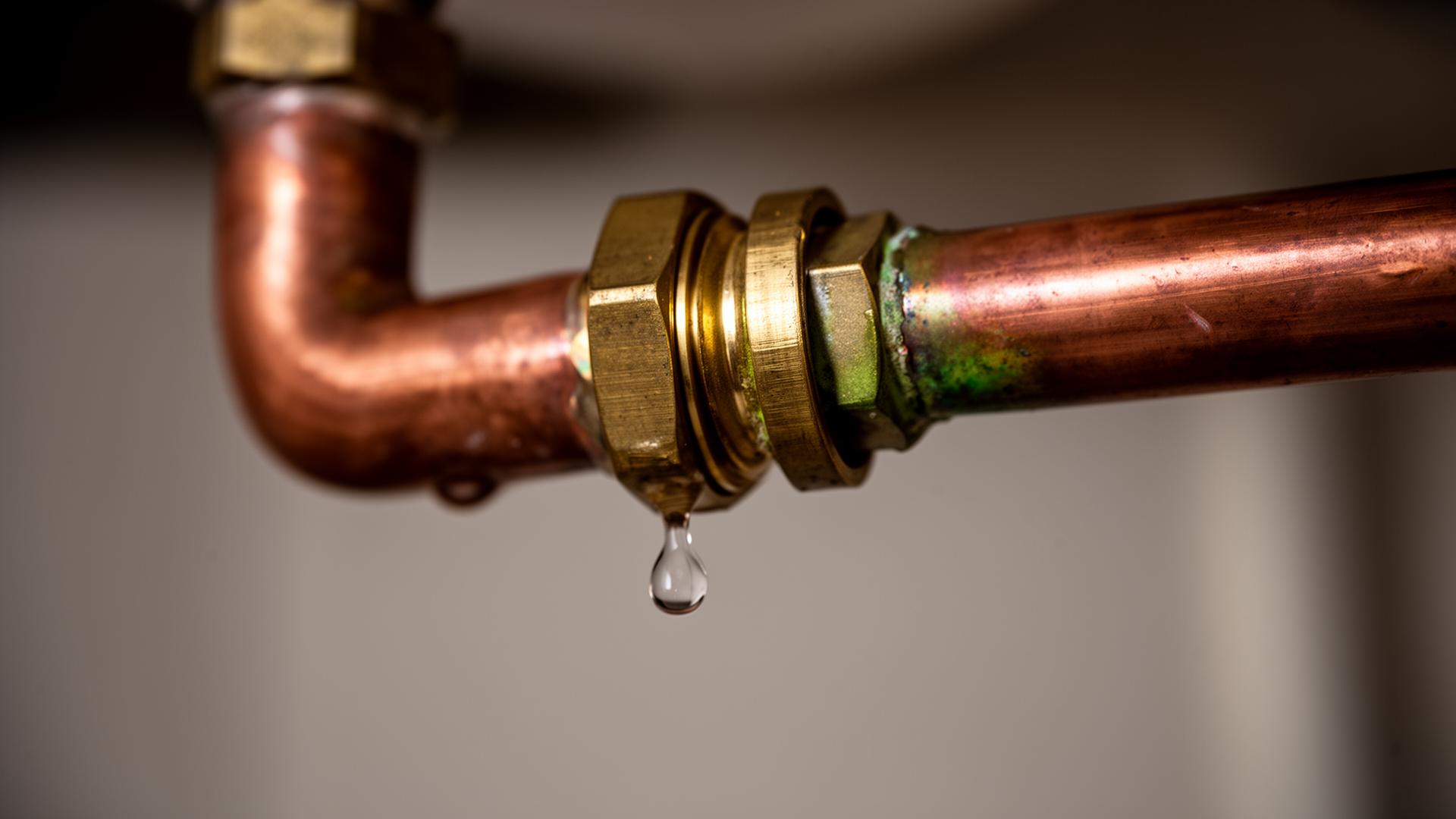 Macro view of a copper pipe joint with a water droplet about to fall from a brass compression fitting